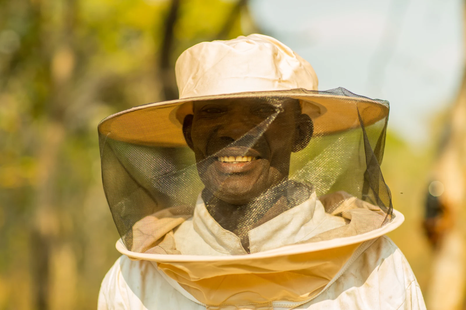 A smiling beekeeper wearing a protective suit and veil